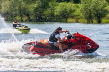 Krasnodar, Rusya - 25 Temmuz 2020: Genç mutlu Kafkasyalı kadın gün batımında kırsal kesimde nehir kıyısında jet ski sürüyor. Ekstrem sporlar ve aktif tatil kavramı