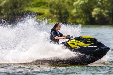 Krasnodar, Rusya - 25 Temmuz 2020: Genç Kafkasyalı kadın, gün batımında kırsal kesimde nehir kıyısında BRP Sea-Doo jet ski sürüyor. Ekstrem sporlar ve aktif yaz tatili konsepti