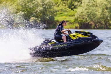 Krasnodar, Rusya - 25 Temmuz 2020: Genç Kafkasyalı kadın, gün batımında kırsal kesimde nehir kıyısında BRP Sea-Doo jet ski sürüyor. Ekstrem sporlar ve aktif yaz tatili konsepti