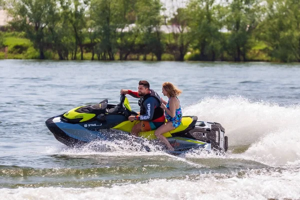 Krasnodar, Rusya - 25 Temmuz 2020: Arka koltukta mutlu bir kadınla erkek binici, gün batımında nehir kıyısında kırsal kesimde BRP Sea-Doo jet su aracını sürüyor. Ekstrem sporlar ve yaz aktiviteleri konsepti