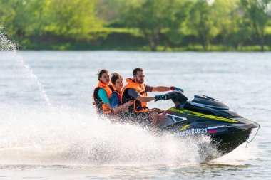 Krasnodar, Rusya - 25 Temmuz 2020: Kırsal kesimde nehir kıyısında güneş batarken jet ski süren mutlu aile. Ekstrem sporlar ve aktif aile yaz tatili konsepti