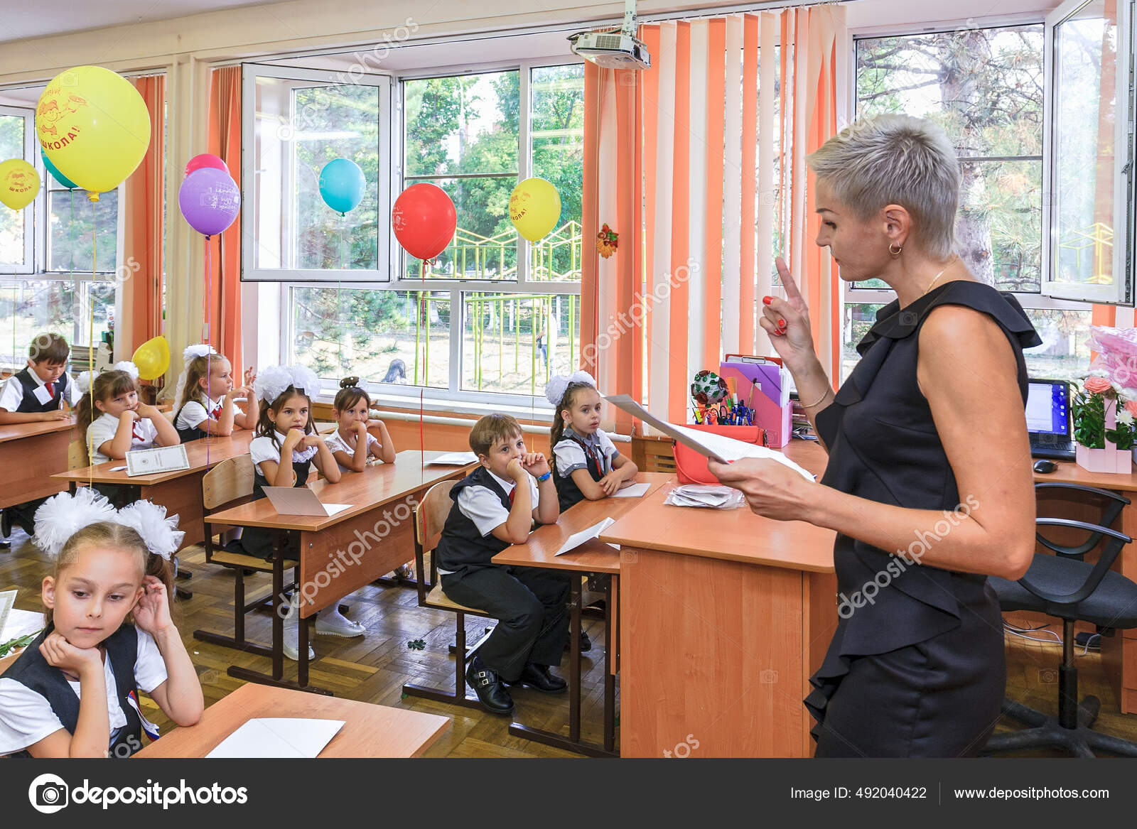 ロシア クラスノダール 2018年9月1日 小学校教育開始の休日に学校の机の上で教室で最初の形の子供たち 女性教師は子供のための最初の学校クラスを実行します  — ストック編集用写真©EvgeniiDikii#492040422, image size:1600x1167