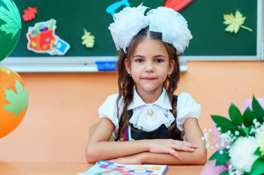 Krasnodar, Rusya - 1 Eylül 2018: İlkokul eğitiminin başlamasıyla ilgili tatilde okul masasının önündeki sınıftaki birinci sınıf öğrencisi mutlu. Birinci sınıf okul.