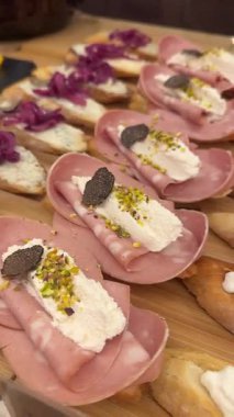 Tahta bir tahtanın üzerinde farklı İtalyan aperatifleri sergilenir. Tahtada etler, peynirler ve çeşitli malzemeler yer alıyor. İnsanlar bu atıştırmalıkların keyfini çıkarabilir..