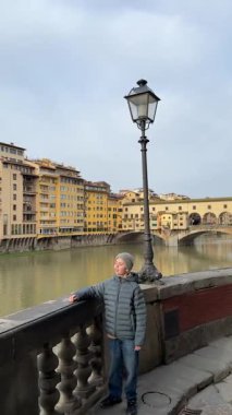 İtalya, Floransa 'da nehrin kıyısındaki taş bir duvarda bir çocuk duruyor. Binalar ve köprü arkasındayken çocuk suya bakıyor. Gökyüzü bulutlu ve sakin..