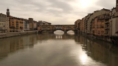 Arno Nehri Floransa 'dan usulca akar. Köprüler nehir boyunca uzanan binalar gibi her iki tarafı da birbirine bağlar. Gökyüzü bulutlu ve ışık suya yansıyarak sakin bir atmosfer yaratıyor..
