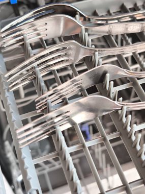 Bulaşık makinesinin çatal bıçak sehpasında yerleştirilen gümüş çatallara odaklanan bir makro çekim.