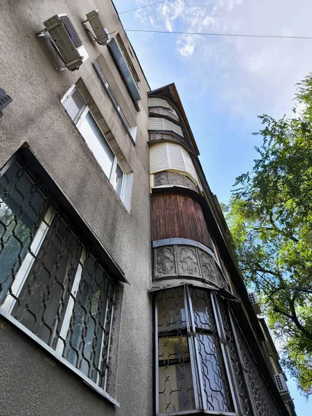 Aşağıdan mavi gökyüzüne bakan, klimalı ve parmaklıklı pencereli Sovyet tarzı bir ev.