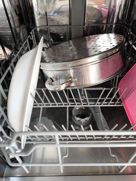 Mutfak malzemeleriyle dolu açık bir bulaşık makinesinin alt rafında büyük paslanmaz çelik, çok katlı bir buhar tenceresi var.