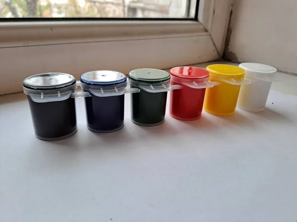 Parlak birincil ve ikincil renklerden oluşan altı küçük, birbirine bağlı konteynır, yaratıcı sanatsal çalışmalar için hazır, parlak bir pencere eşiğinde otururlar.