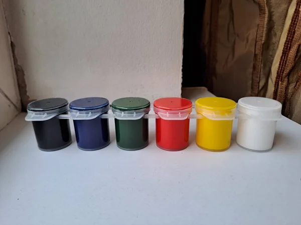 Parlak birincil ve ikincil renklerden oluşan altı küçük, birbirine bağlı konteynır, yaratıcı sanatsal çalışmalar için hazır, parlak bir pencere eşiğinde otururlar.