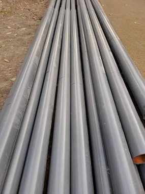 Toprak ve beton yol kenarında kurulum ya da taşınmaya hazır birkaç büyük, gri metal borunun yakın çekimi.
