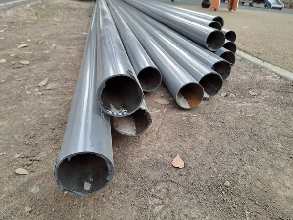 Toprak ve beton yol kenarında kurulum ya da taşınmaya hazır birkaç büyük, gri metal borunun yakın çekimi.