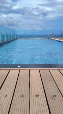 Yüksek katlı terasta modern bir yüzme havuzu. Ahşap döşeme ve parlak bir günde deniz manzaralı bir arka plan.
