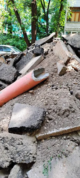 Yüksek açılı yıkım manzarası içinde asfalt parçaları, kir ve inşaat alanındaki hasarlı turuncu plastik boru da var.