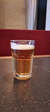 Koyu bir kafe masasında duran bir bardakta servis edilen ferahlatıcı bir alkollü içecek.