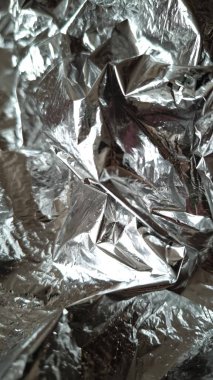 Metalik yansımaları ve gölgeleri olan buruşmuş gümüş alüminyum folyonun soyut dokusu