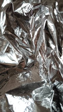 Metalik yansımaları ve gölgeleri olan buruşmuş gümüş alüminyum folyonun soyut dokusu