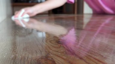 Islak ahşap masa yüzeyini dezenfeksiyon için beyaz bezle silen biri.
