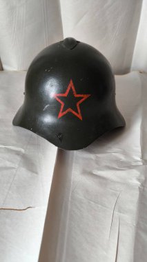 Kırmızı yıldız sembollü klasik askeri çelik miğfer. Yeşil metal asker miğferi, arka planda kırmızı bir yıldız var. Ordu korumasını ve askeri tarihi temsil eden tarihi eser.