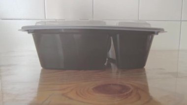 Tahta Masa 'ya boş plastik yiyecek konteynırı. Yemek hazırlamak ya da paket servis etmek için açık bir kapağı olan tek kullanımlık siyah iki kompartıman fotoğrafı.