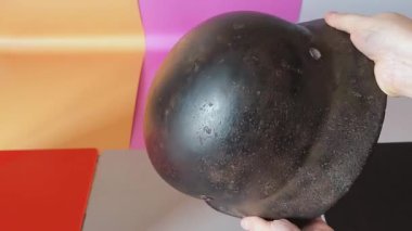 Hasar ve dokuları göstermek için elleri paslanmış savaş miğferini döndürüyor. Tarihi çalışmalar için paslanmış ve iç yapısını gösteren otantik yıpranmış çelik bir miğfer..