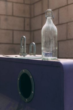 Şişedeki çöp kutusunda cam şişe var. Yeşil kavramı takip ederek atığı azaltmak. Geri dönüşüm süreci. Kirli açık hava şişesi, gündüz görüşü, arka planda kahverengi duvar.