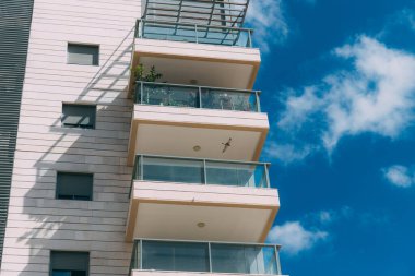Balkonlar ve bulutlu mavi gökyüzü. İsrail 'de bir yerleşim yerinin parçası. Güneşli bir günde modern apartman binaları. Mimari detaylar. Balkonlu modern beyaz bina. 