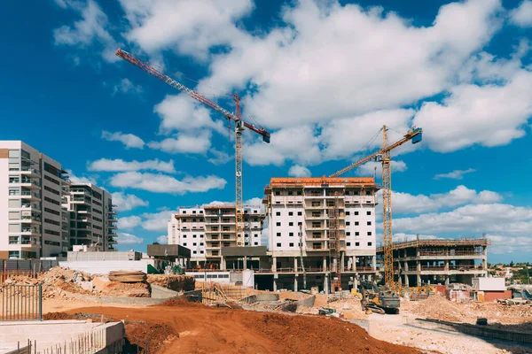 Vinçleri ve kazıcısı olan inşaat alanı, mavi gökyüzü arka planında kum. İsrail 'de insanlar için yeni evler inşa ediyoruz. Şehirdeki ev inşaatı. 