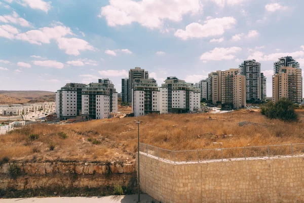 Yeni binalar. İsrail 'in doğusunda birçok yeni ev. Bulutlu mavi gökyüzüne karşı yerleşim binaları. Kahverengi kavrulmuş ot. Çok katlı binalar. 