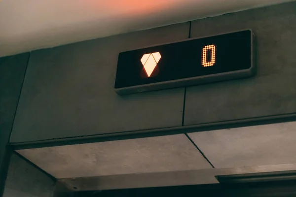 Elevator floor display screen. Monitor show orange number zero floor and arrow down in elevator.