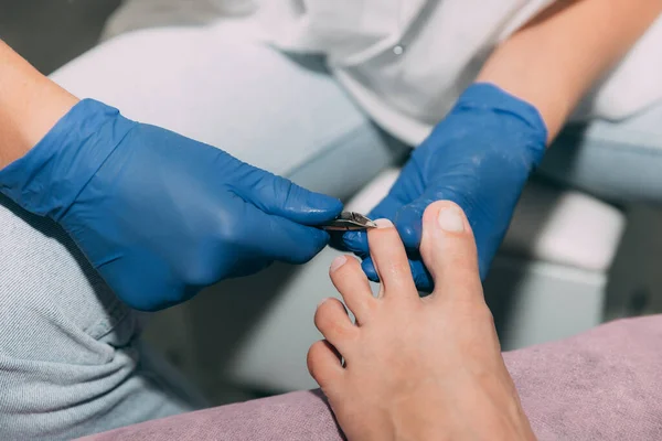 Pedicure process in salon. Foot care treatment and nail. Removing dead skin with forceps. Master in blue gloves makes pedicure with manicure machine. Concept of beauty care and health.