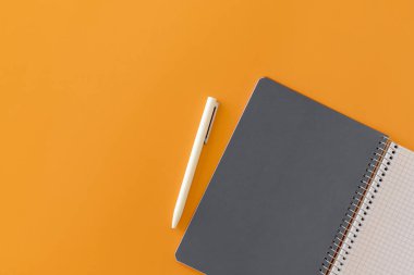 Spiral, gri sayfa ve beyaz kalemle defter açtı. Turuncu arkaplanda metin için düz ve yerleşik bir yer. Okula dönelim. Üst görünüm, boşluğu kopyala. Yüksek çözünürlük Öğrenci işyeri