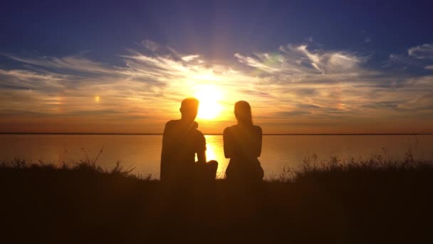 Romantiska par njuter av solnedgången sitter på stranden och kramas första oskärpa — Stockvideo