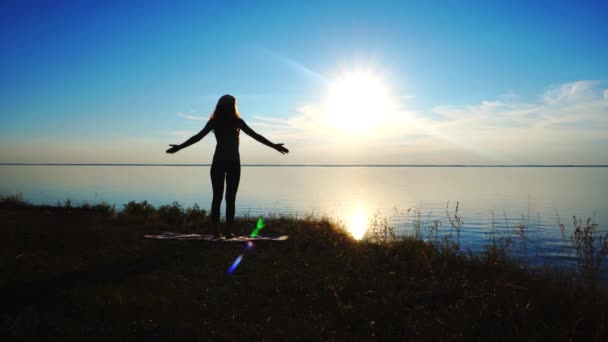 Siluett kvinna gör en krigare yoga posera vid solnedgången på stranden — Stockvideo