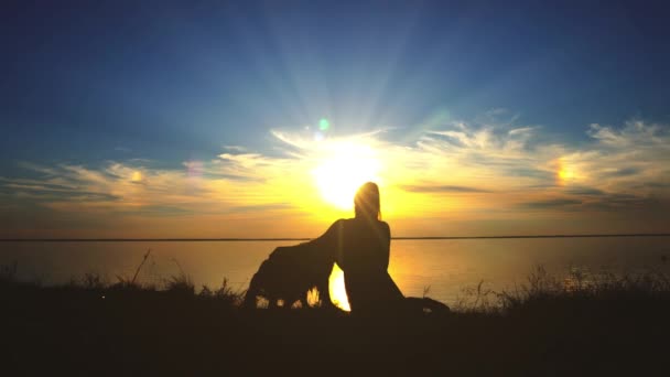 女性がビーチで夕暮れ時彼女の犬を抱擁します。 — ストック動画