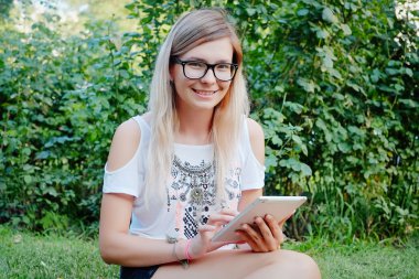 tablet ellerde ile çimlerde oturan kız