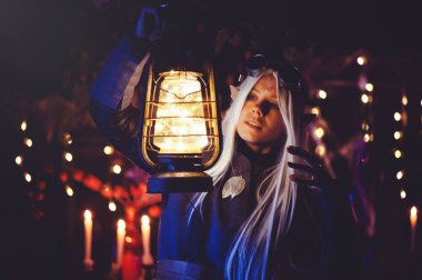 Karanlık ormanda sihirli büyüleri olan Cadılar Bayramı elfi. Şapkalı ve elf kostümlü güzel genç bir kadın sihirli bir kimya tutuyor. Cadılar Bayramı Sanat Tasarımı