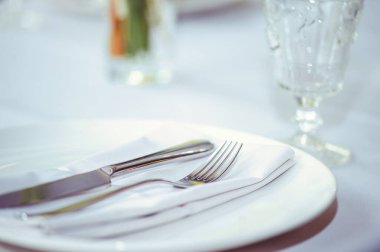 Beyaz tabak ve gümüş çatal bıçaklı restoran masası takımı..