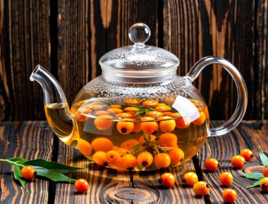 Sıcak sonbahar atmosferi, buharı tüten deniz dikenli çay, koyu ahşap masada bağışıklık kazanmak için ısınan vitamin içeceği..