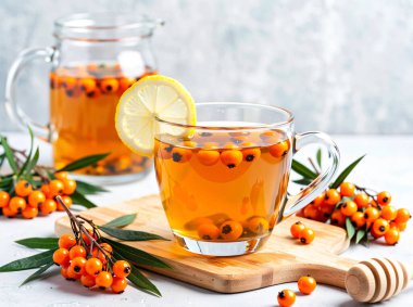 Taze limon dilimi ve parlak böğürtlen dalıyla süslenmiş buharda pişmiş bir deniz dikenli çay. Bu şifalı bitkisel karışım beyaz bir peçeteye ısı, rahatlık ve bağışıklık desteği sağlar..