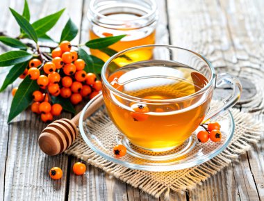 Kırsal bir ahşap masaya konmuş, buharı tüten bir bardak karabatak çayı. Taze portakal meyveleri ve yeşil yapraklarla çevrili bu canlı bitkisel karışım doğal ısı ve vitamin enerjisi yayar..