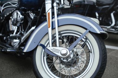 Beyaz çizgili metalik mavi çamurluk, klasik bir beyaz duvar lastiği, cilalanmış krom telli tekerlekler ve ön çatallar içeren klasik model bir motosiklet ön ucu..