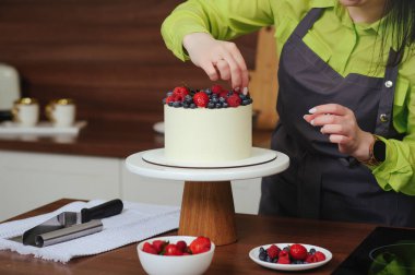 Pasta şefi, beyaz kremalı pastayı taze böğürtlenlerle süslüyor.