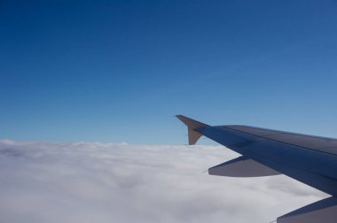 Kalın bir bulut örtüsünün üzerinde bir uçak kanadı görünüyor.