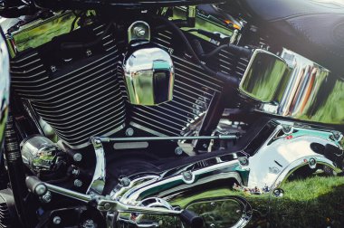 V-ikiz motorlu parlak krom motorun yatay yakın çekimi. Cilalı yüzeyler bir bisiklet fuarındaki yeşil çimenleri ve dışarıdaki çevreyi yansıtıyor..