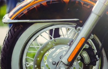 Özel bir motosikletin ön tekerleğinin yatay yakın çekimi, bozuk bir jant, fren diski ve boyalı bir çamurluğun altında beyaz bir lastik..