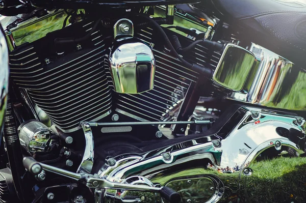 V-ikiz motorlu parlak krom motorun yatay yakın çekimi. Cilalı yüzeyler bir bisiklet fuarındaki yeşil çimenleri ve dışarıdaki çevreyi yansıtıyor..