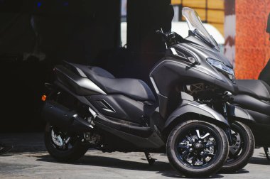 Büyük bir ön cam, aerodinamik kaporta ve siyah alaşımlı jantlar içeren parlak, koyu gri üç tekerlekli bir mobiletin yan profili..