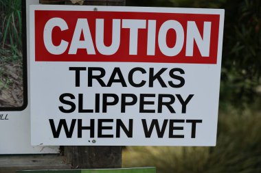 Kalın uyarı tahtası çevreleyen yeşilliklerin yanında duruyor. Tehlike işareti.